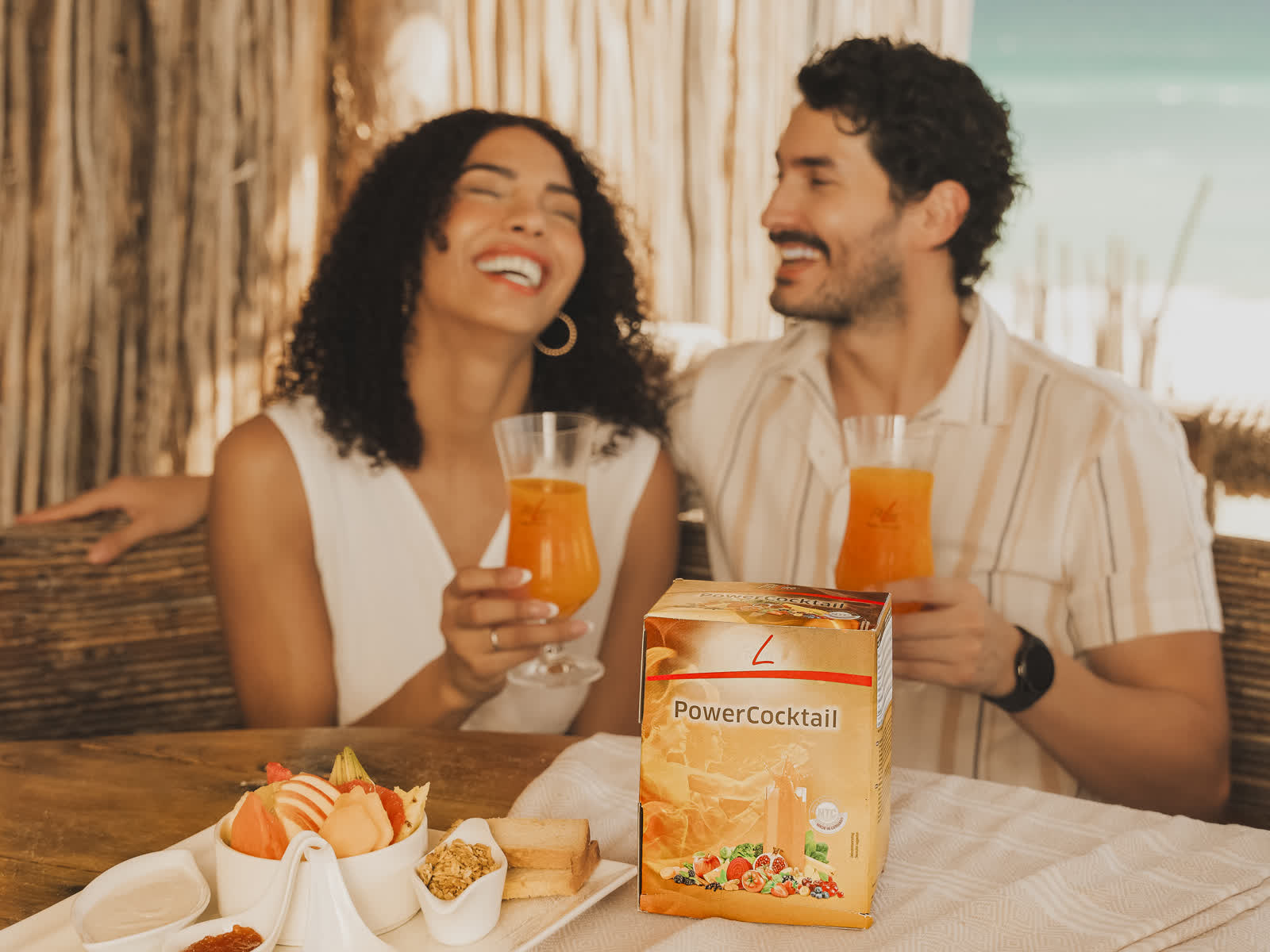 Упаковка FitLine PowerCocktail на столе, за ней люди с напитками
